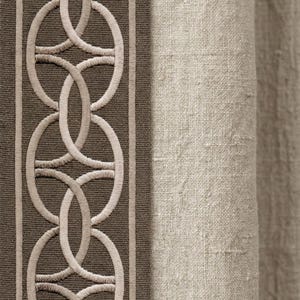 May include: Close-up of a fabric panel featuring a decorative border with an embroidered interlocking circle design in beige on a dark brown background. The right side shows a beige linen fabric.