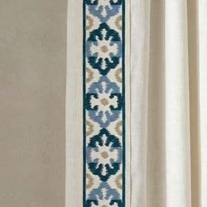 Può includere: Pannello tenda bianco sporco con bordo ricamato verticale. Il bordo presenta un motivo ripetuto di motivi floreali verde acqua, azzurro e beige. La tenda è realizzata in un tessuto strutturato e lo sfondo è di colore neutro.