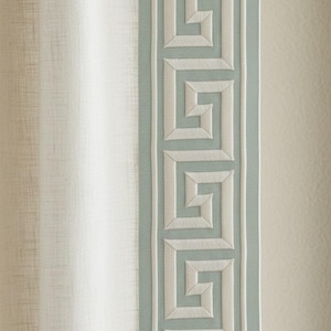 May include: Close-up of a decorative fabric panel featuring a Greek key design. The panel has a light blue border with a repeating white geometric pattern. The background is a light beige color.
