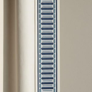 May include: Close-up of a cream-colored curtain with a vertical border. The border features a geometric pattern in shades of blue and white. The curtain is made of a textured fabric.