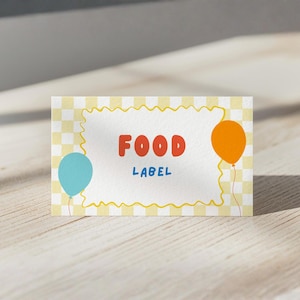 May include: A rectangular food label card featuring a light yellow and white checkered background. The center has a white area with a yellow wavy border, the red text FOOD, the blue text LABEL, a light blue balloon, and an orange balloon.