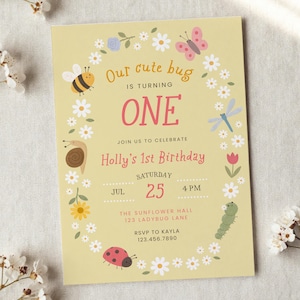 May include: A rectangular birthday invitation card on a light yellow background featuring a floral wreath border with illustrations of a bee, butterfly, snail, dragonfly, caterpillar, and ladybug. Text reads: Our cute bug is turning ONE, Holly's 1st Birthday, Saturday, July 25, 4 PM, The Sunflower Hall, 123 Ladybug Lane, RSVP to Kayla 123.456.7890.