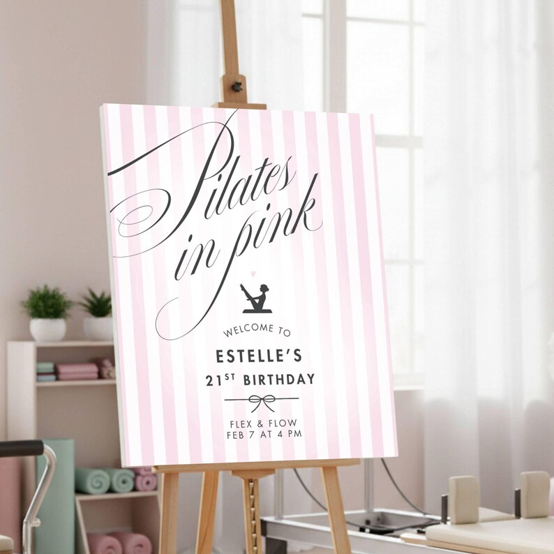 May include: A pink and white striped sign on a wooden easel. The sign reads "Pilates in Pink" in elegant script, with additional text below indicating a birthday celebration. The sign includes a bow graphic and the words "Flex & Flow".