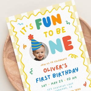 May include: A first birthday invitation card featuring a light yellow checkered background with a wavy yellow border. The text reads IT'S FUN TO BE ONE, JOIN US TO CELEBRATE OLIVER'S FIRST BIRTHDAY, SAT MAY 23 10 AM, 123 SUNSHINE LANE, SUNNYBROOK, CA.