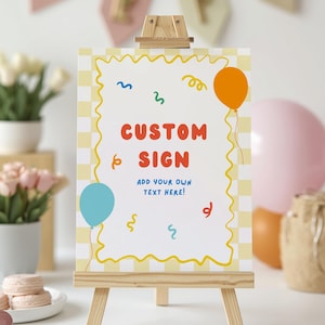 May include: A rectangular sign on a wooden easel featuring a white center with a yellow wavy border and a light yellow checkered background. The sign displays the red text CUSTOM SIGN and blue text ADD YOUR OWN TEXT HERE, with colorful balloons and confetti.