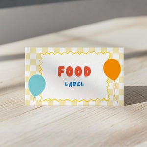 May include: A rectangular food label with a yellow gingham background and a wavy yellow border. The words "FOOD LABEL" are in red and blue, with a blue and orange balloon on either side.