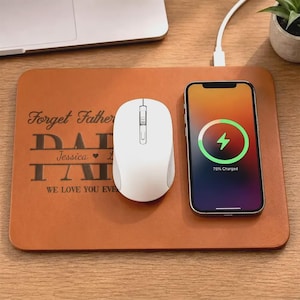 May include: A brown leatherette desk mat with the text "Forget Father DAD I LOVE YOU EVER" and a white wireless mouse. A smartphone is charging on the mat, displaying a charging icon and 75% charged.