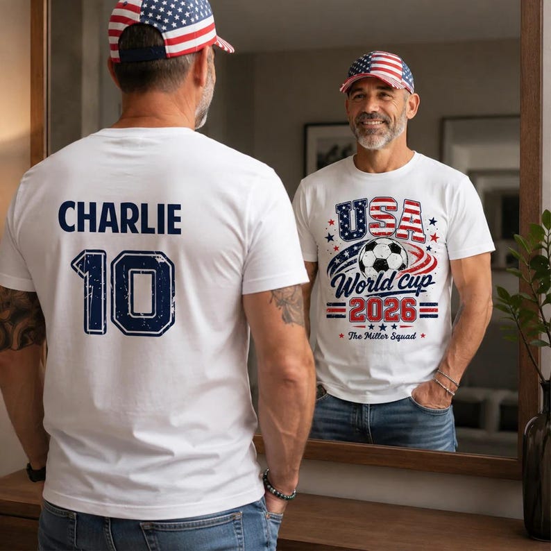Op de afbeelding: Een wit t-shirt met de naam CHARLIE en het nummer 10 in marineblauw op de achterkant. De voorkant toont een afbeelding met een voetbal, de tekst USA World cup 2026 en The Miller Squad. Een bijpassende honkbalpet met vlag is gedragen.
