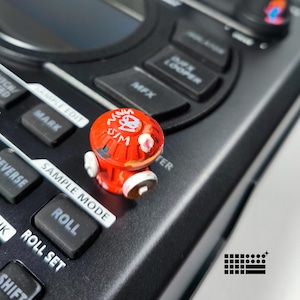 May include: A red and white miniature fire hydrant figurine with graffiti-style art. The figurine is placed on a black electronic device with buttons labeled "Sample Edit", "Roll", and "Reverse".