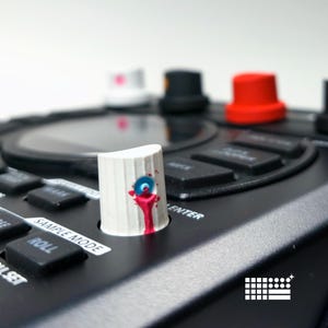 Puede incluir: Primer plano de un dispositivo electrónico negro con varias perillas y botones de colores. Una perilla blanca con un diseño azul y rojo está enfocada. El dispositivo tiene etiquetas como "SAMPLE MODE" y "ENTER".