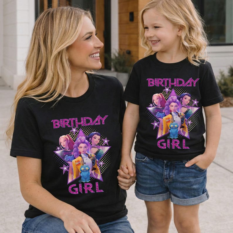 May include: Two black t-shirts with the text "BIRTHDAY GIRL" in pink glitter. The shirts feature a graphic of animated characters within a star shape. The shirts are worn by a woman and a young girl.