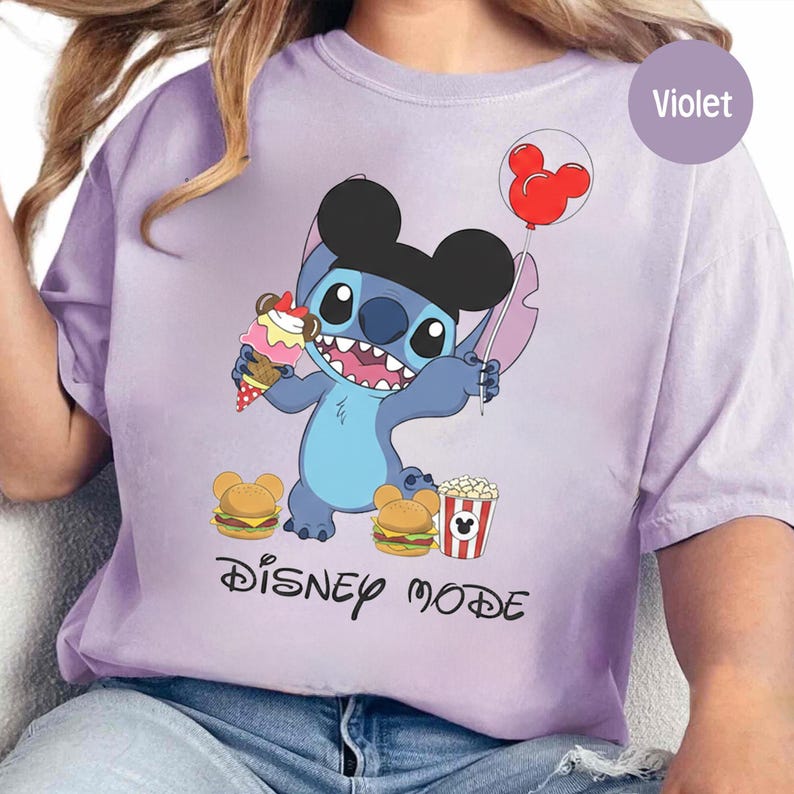 A person wearing a purple t-shirt with a cartoon character from the Disney movie Lilo and Stitch, along with various Disney-themed items such as popcorn and a Mickey Mouse balloon.