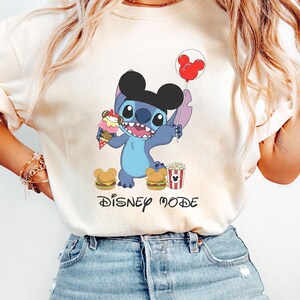 A person wearing a white t-shirt with a cartoon character and text related to Disney.