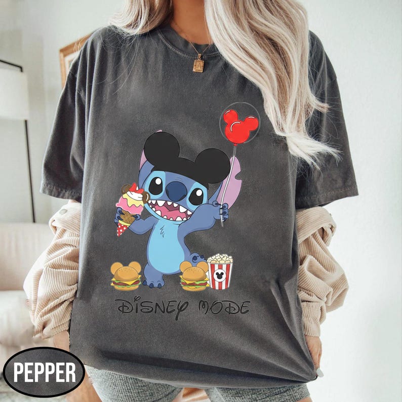 A person wearing a gray t-shirt with a graphic of a cartoon character and various Disney-themed items, such as Mickey Mouse and popcorn.