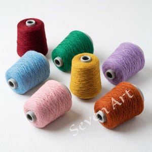 Puede incluir: Una colección de coloridos conos de hilo en tonos rojo, verde, azul, amarillo, morado, rosa y naranja. El hilo está enrollado firmemente en conos de cartón con inserciones de plástico gris. La imagen está bien iluminada, mostrando la textura y los colores vibrantes del hilo.