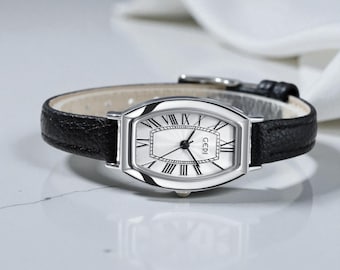 May include: A silver-toned wristwatch with a rectangular face and black leather band. The watch face is white with black Roman numerals and the brand name "GEDI". The band is approximately 0.5 inches wide.