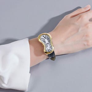 May include: A gold-toned wristwatch with a melting, curved case design. The watch face is white with black Roman numerals and a zebra-striped center. It has a black leather band, creating a surreal and artistic aesthetic.