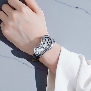 May include: A silver-toned wristwatch with a melting, curved face and black Roman numerals. The watch has a black leather band and is worn on a wrist. The watch face has a white background with black lines and Roman numerals.
