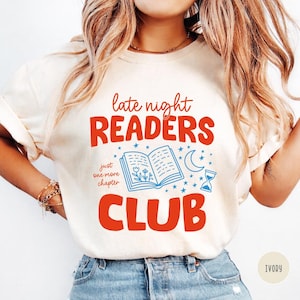 May include: Ivory-colored t-shirt with the text "late night READERS CLUB" in red and blue. The design includes an open book, stars, a crescent moon, and an hourglass. The phrase "just one more chapter" is also included.