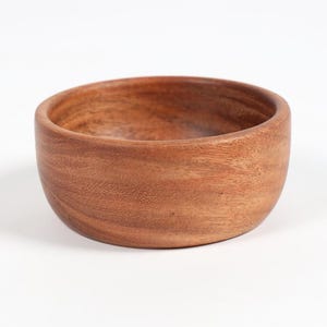 May include: A round, wooden bowl with a natural, warm brown color. The bowl has a smooth, curved design and a simple, minimalist aesthetic. The wood grain is visible, adding texture and character to the piece. Perfect for serving or as a decorative accent.