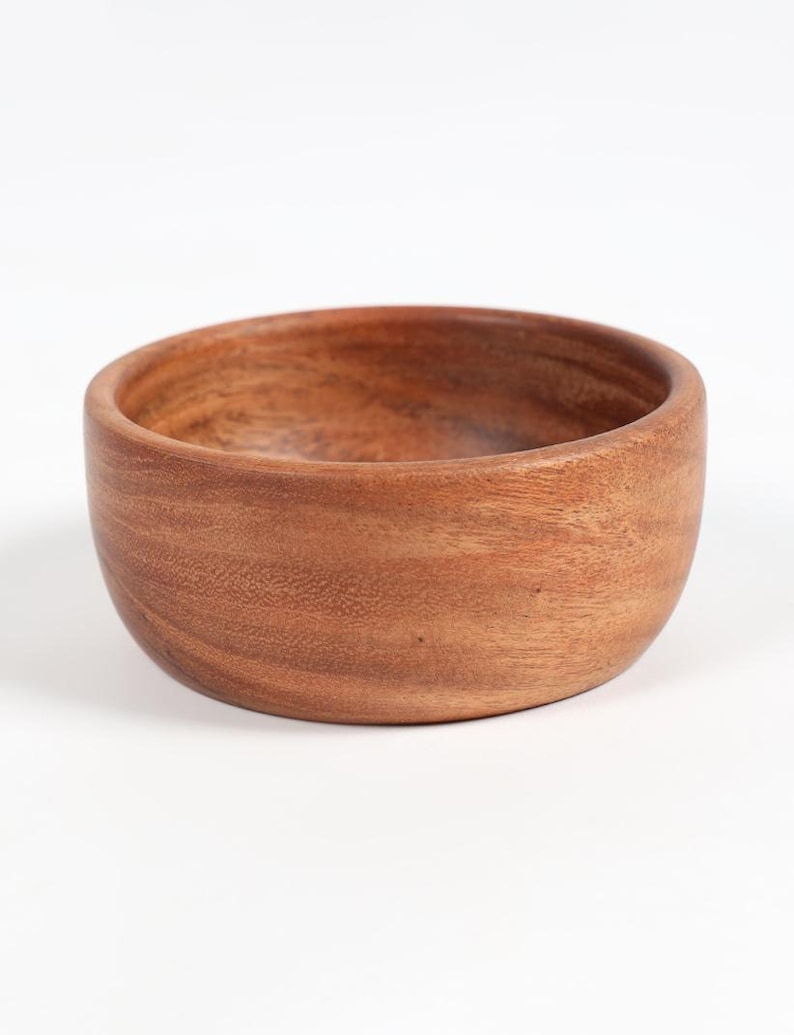May include: A round, wooden bowl with a natural, warm brown color. The bowl has a smooth, curved design and a simple, minimalist aesthetic. The wood grain is visible, adding texture and character to the piece. Perfect for serving or as a decorative accent.