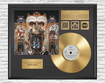 May include: A framed display featuring the Michael Jackson Dangerous album cover art, a gold-colored vinyl record, and a gold plaque with the text YOUR NAME. The display includes a QR code, a small image, and a gold PGA logo on a black background.