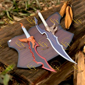 May include: Two decorative swords with ornate designs. One sword features a red and black blade with an orange hilt, while the other has a blue blade and gold accents. Both are displayed on wooden plaques.
