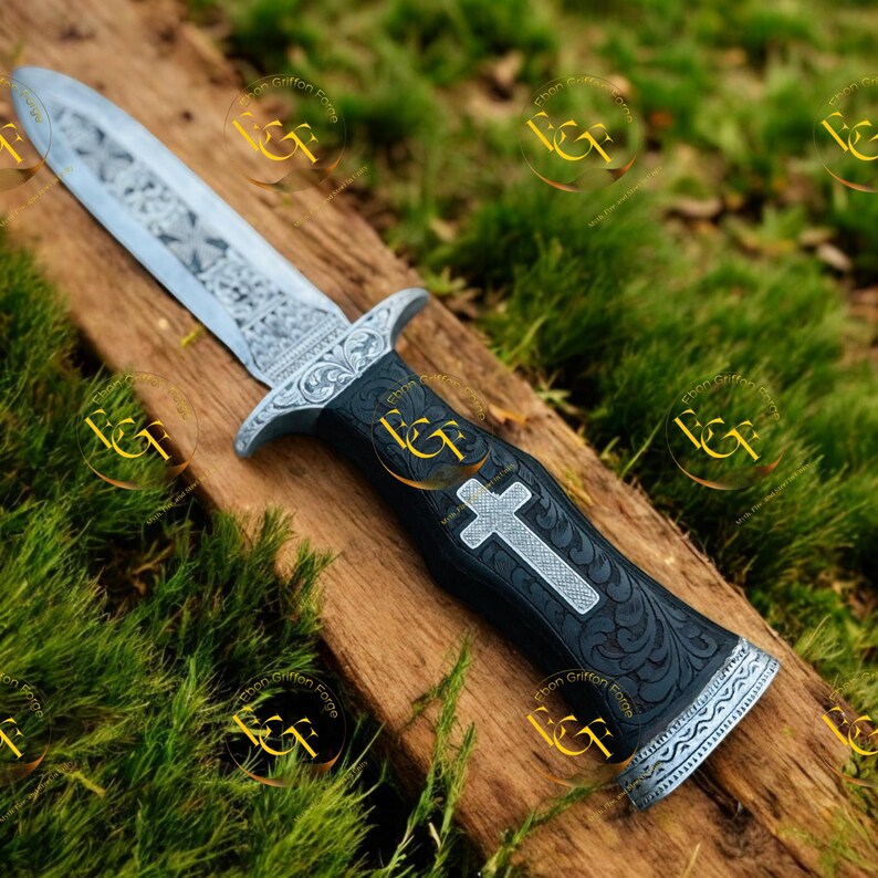 May include: A decorative dagger with an engraved silver blade and a black handle. The handle features a silver cross and ornate floral patterns. The dagger is displayed on a wooden surface with a green background.