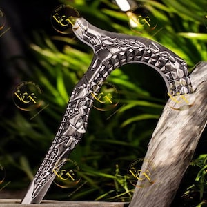 May include: A silver walking stick with an ornate, geometric pattern on the handle and upper shaft. The stick is propped against a piece of weathered wood, with a blurred green backdrop.