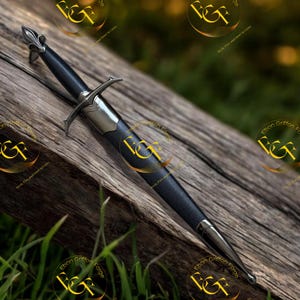 May include: A dagger with a black textured grip and a silver-toned metal crossguard featuring a fleur-de-lis pommel. The weapon is encased in a matching black scabbard with silver-toned metal fittings at the throat and the pointed tip.
