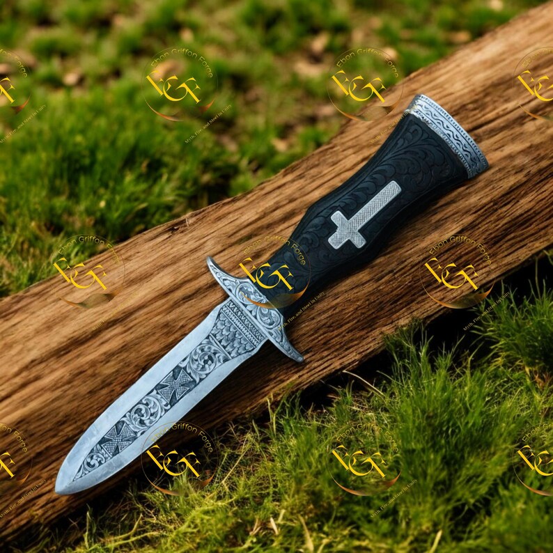 May include: A decorative dagger with a silver blade and ornate handle. The handle is black with a silver cross design. The blade features detailed engravings. The dagger rests on a wooden surface against a backdrop of green grass.