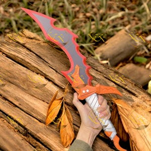 May include: A fantasy sword with a red and gray blade, orange accents, and a white and silver wrapped handle. The sword is held against a backdrop of wood and leaves.