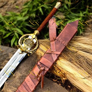 May include: A decorative sword with a gold hilt and a brown leather-wrapped handle. The blade is silver and the sword is accompanied by a brown leather sheath. The sword has an ornate design and is likely for display or cosplay.