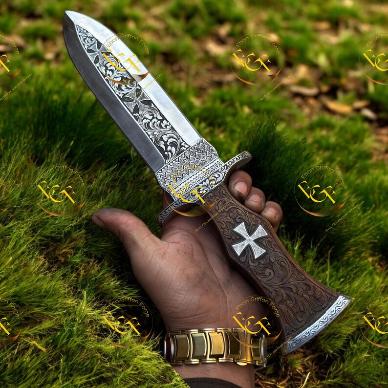 May include: An ornate dagger with a silver blade and a wooden handle. The blade features intricate engraved patterns. The handle has a cross design and is held in a hand. A gold bracelet is visible on the wrist.