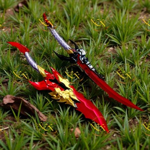 May include: Two fantasy swords with red and gold blades, and silver and black handles, rest on a bed of green grass. The blades have intricate designs and the handles feature ornate details. The swords appear to be decorative or for cosplay.