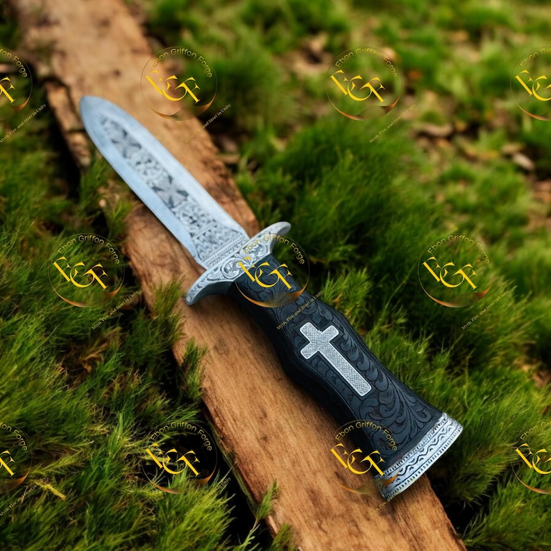 May include: A decorative dagger with an ornate silver blade and a black handle. The handle features a silver cross and decorative patterns. The dagger rests on a wooden surface against a backdrop of green foliage.