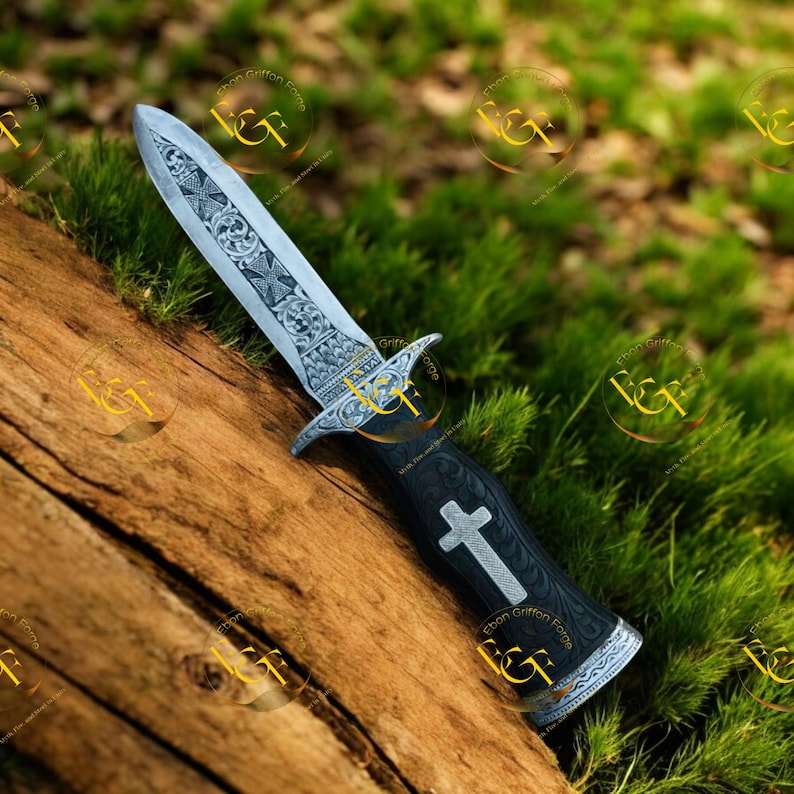 May include: A decorative dagger with an ornate, engraved blade and a black handle. The blade features detailed patterns, and the handle has a white cross design. The dagger rests on a wooden surface with a green, grassy background.