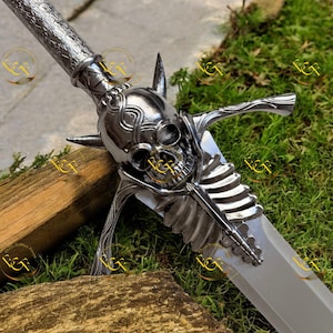 May include: A silver-colored fantasy sword with a skull-shaped hilt and a blade. The hilt features a detailed skull design with spikes and a ribcage motif. The blade is a light silver color, and the sword is set against a backdrop of green foliage.