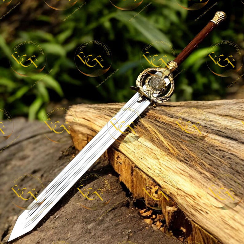 May include: A decorative sword with a silver blade and a brown handle. The hilt features gold-colored accents and a circular design with a central stone. The sword is displayed on a piece of wood.