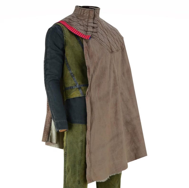 May include: A multi-layered garment featuring a brown cape, a quilted collar, and a green and blue vest. The cape has a frayed edge and a red accent. The outfit appears to be made of durable, textured fabric.