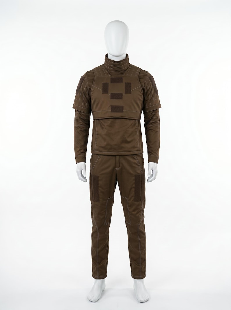 Pode incluir: Um uniforme t&aacute;tico castanho exibido em um manequim. O conjunto inclui uma parte superior de manga comprida com gola alta e peitoral, e cal&ccedil;as a condizer. Apresenta remendos e costuras refor&ccedil;adas.