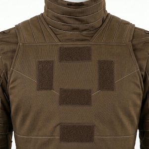 Pode incluir: Um colete t&aacute;tico castanho com gola alta e v&aacute;rios patches de velcro. O colete tem um design acolchoado com costuras brancas e &eacute; exibido em um manequim.
