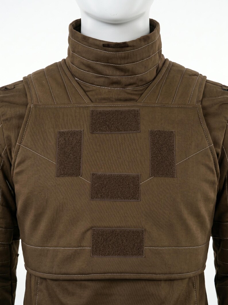 Pode incluir: Um colete t&aacute;tico castanho com gola alta e v&aacute;rios patches de velcro. O colete tem um design acolchoado com costuras brancas e &eacute; exibido em um manequim.
