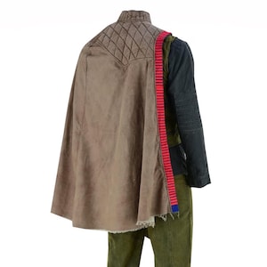 May include: A brown cape with a quilted shoulder detail and a red and blue strap. The cape is paired with a dark green and black jacket and green trousers. The outfit has a distressed, worn appearance.