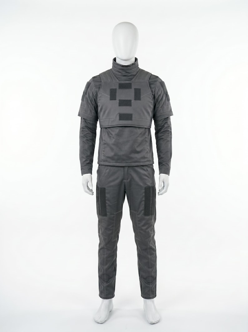 May include: A gray tactical uniform displayed on a mannequin. The outfit includes a long-sleeved shirt with a high collar, a vest with square patches, and matching pants. The uniform is designed for protection and features reinforced areas.