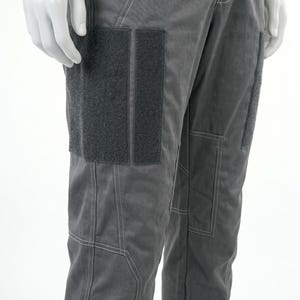 May include: Close-up of gray pants with visible stitching and two dark gray rectangular patches on the left thigh. The pants have a utilitarian design, with a pocket on the right thigh. The fabric appears to be a durable, possibly workwear material.