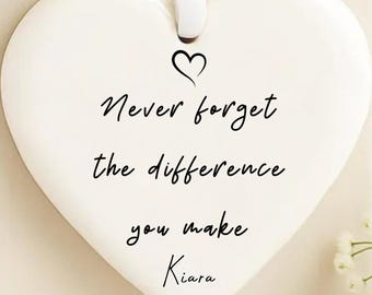May include: A white heart-shaped ceramic ornament with a black heart and the inscription "Never forget the difference you make Kiara." A white ribbon is attached for hanging. The ornament is presented on a white gift box.