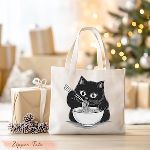 May include: Off-white tote bag featuring a black and white illustration of a black cat eating noodles from a bowl with chopsticks. The words "Zipper Tote" are printed at the bottom. The bag has two white handles and is set against a blurred background.