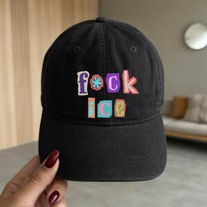 May include: Black baseball cap with the text "f*ck ice" in colorful, block letters. The hat has a curved brim and a classic, adjustable design. The text is in purple, pink, blue, orange, and green.