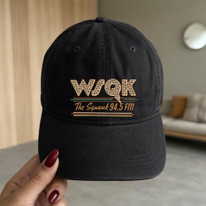May include: Black baseball cap with the text "WSQK The Squawk 94.5 FM" in a leopard print and striped design. The cap has a curved brim and a rounded crown.